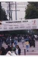 Men and women walk through black gate with banner "Clark Atlanta University, Homecoming 1999, 'Taking It To Another Level.'"