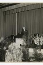 A man stands at a podium at the 75th Anniversary Band Concert.
