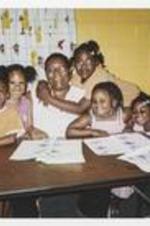 A group of children sit with Carolyn Christian. A young girl, Christian Stembridge has her arms wrapped around Ms. Christian. Written on verso: Vacation Bible School - 2007. Jordan McKnight, [Amiyah] McCoy, Carolyn Christian (adult), Christian Stembridge (w/arm around Carolyn's neck, Kyla-Key Lewis, Makayla Lewis.