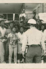 A Birmingham policeman is shown standing in front of a crowd of demonstrators. Caption  on verso: MISCALCULATION COULD MEAN VIOLENCE -- Police reaction to jeering crowds, in either north or south, could result in major racial violence in the U.S. this summer. As this policeman in Birmingham faced a crowd in May of this year, so will other law enforcement officers in other cities face demonstrators. A miscalculation in the handling of a crowd could be the spark that touches off a racial conflagration.
