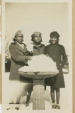 Three girls stand behind a bird feeder filled with snow.