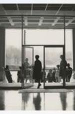 Silhouette view of men and women standing outside of building with glass entryway wall.