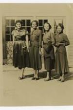 Four women pose in front of a building.