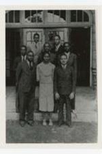 A group portrait of six men and a woman on steps outside of a building.