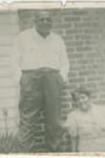 An unidentified woman sits and leans against a brick structure while an unidentified man stands next to her.