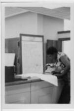 A woman stands at a counter and writes with a map in the background.