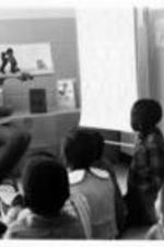 An unidentified woman reads to children in a classroom. Written on verso: Boggs Academy Keysville, GA 30816.