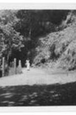 An unidentified woman standing in a road. Possibly in India. Written on verso: to Mama Hall with love. My roommate took this of me coming around the mountain. Notice the "ravine like" drop.