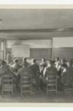 Members of the Science Club sit in a classroom where a man points at a blackboard.