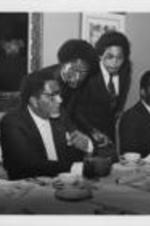 Joseph E. Lowery is shown speaking to E. Randel T. Osburn alongside Evelyn G. Lowery and others at a Southern Christian Leadership Conference Board Luncheon. Written on verso: Discussing a "serious problem"... President Lowery instructs E. Randel T. Osburn and Sevell Brown, III to improvise as SCLC is confronted with larger turnout for board luncheon than anticipated. Awaiting lunch is Mrs. Lowery, Dr. David Swenton, speaker and Rev. Emmanuel Cleaver.