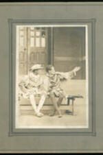 Two men in theater costumes sit on a bench.