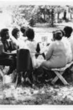 A group of women sit at a picnic table eating cookies.