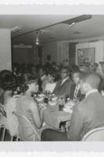 A group of men and women sit at long dining tables.