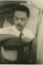 Portrait of Peter Abrahams leaning on the back of a chair. Written on verso: Peter Abrahams; Photograph by Carl Van Vechten; 146 Central Park West; Cannot be reproduced without permission; Nov. 25, 1955.