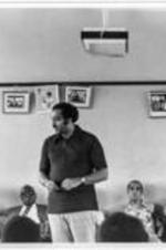 An unidentified man stands amongst a group of people gathered in a room.