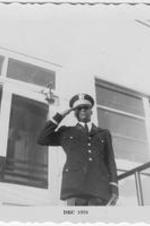 An unidentified man in military regalia salutes outside of a building.