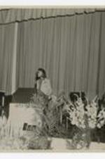 A woman stands at a podium at the 75th Anniversary Band Concert.