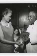 Grace Towns Hamilton with Dr. Paul I. Gifford holding a  plaque. Written on verso: A.U. Alumni Assoc. plaque presented to Mrs. Grace (Towns) Hamilton by Dr. Paul I. Clifford, in background, left of Dr. Clifford, Mrs. Tobin, teacher in Atlanta Schools (high school).