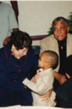 Evelyn G. Lowery smiles at a toddler that she holds in her arms while Joseph E. Lowery looks on.