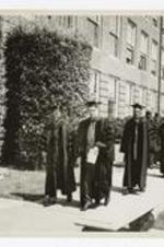 James P. Brawley and another man lead the academic procession past a brick building at commencement.