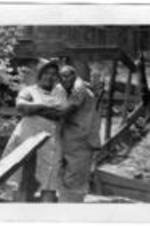 An unidentified couple share a loving embrace. Behind the couple is wooden scaffolding and stilts for houses.