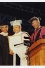 Wynton Marsalis, Thomas W. Cole, Jr. and another man, wearing a graduation cap and gowns, stand at the podium at commencement.