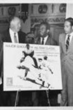 Southern Christian Leadership Conference President Ralph D. Abernathy is shown with others standing around a poster advertising the Major League E-W All Star Classic Game to be held in memory of Martin Luther King, Jr. Written on verso: Press Conference, from left to right: Rev. H.H. Brookins (SCLC West), A.E. Patterson (Vice Pres, Public Relations), Rev. Ralph D. Abernathy, George Lederer (Dir. Of Promotion, Calif. Angels), Rev. Andrew Young