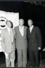 Floyd Flake and L. Henry Whelchel stand on stage with an unidentified man.