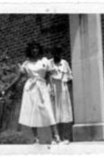 Unidentified girls in white dress stand in front of a brick building.