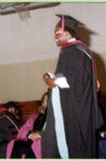 An unidentified graduate stands on stage in front of platform participants.