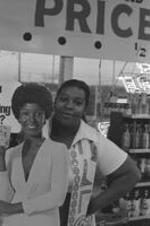 An unidentified woman stands beside an advertising cutout in a liquor store.