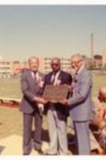 President Hugh Gloster with unidentified persons holing a plaque at the Morehouse stadium. Written on verso: Dedication of B.T. Harvey Stadium 9/24/83.