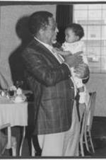 Joseph E. Lowery stands at a banquet event holding a baby.