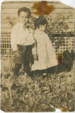 Two children stand together outside.