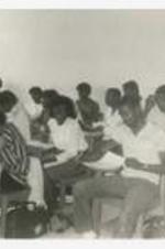 Indoor view of young men and women in classroom seated at desks.