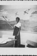 An unidentified woman holding a yard stick points to a bulletin board mural.