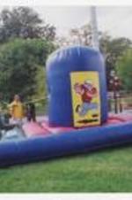 Two young people stand on an inflatable football-themed bounce house on campus.