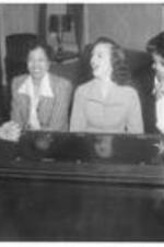 Four women sing at a piano. Written on verso: Students in dormitory, 1951. Smith, Mayberry, Carroll, and Samuel.