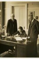View of President Florence Matilda Read signing document at desk with John Hope looking on. Written on verso: President Read (middle) - the signing of the Affiliation Agreement amongst Morehouse College, Spelman College, and Atlanta University - April 1, 1929.