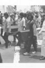 A group of men carry two coffins in the March Against Repression. Written on accompanying document: Scenes of the March in Progress.
