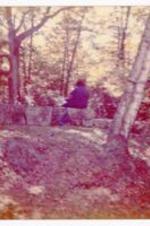 Unidentified person sitting on a campus area. Written on verso: Beth meditating in Bird's Sanctuary at Phillip's (Note the popular New England Branches) Oh! Robert Frost.