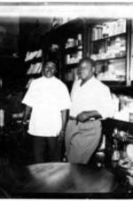 Two unidentified men stand in a pharmacy.