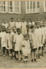 A large group of children gather outside in a formation.