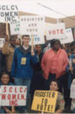 Evelyn G. Lowery is shown speaking to a crowd while surrounded by SCLC/W.O.M.E.N. Civil Rights Heritage Tour participants holding signs advocating for voting and voter registration.
