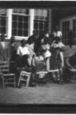 View of an unidentified group standing outside caning chairs.