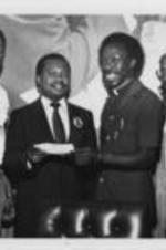 Southern Christian Leadership Conference staff member E. Randel T. Osburn presents a $1,000 check to Carl McNair, the brother of astronaut Ron McNair, who died in the Space Shuttle Challenger explosion. Written on verso: On behalf of the president... SCLC administrator, Rev. Albert E. Love and Coordinator of Direct Action Rev. Fred D. Taylor look on as Carl McNair receives $1000 check presented by E. Randel T. Osburn on behalf of Dr. Joseph Lowery.