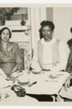 Women sit in a living room around a breakfast table. Written on verso: Alumni Breakfast, June 1954.