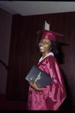 An unidentified young woman in a cap &amp; gown holds her diploma under her arm.