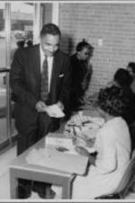 Joseph E. Lowery is shown talking to a woman with a typewriter while smiling and holding a booklet.