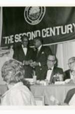 View of two men at a podium. Banner reads, "Morehouse College, The Second Century"
